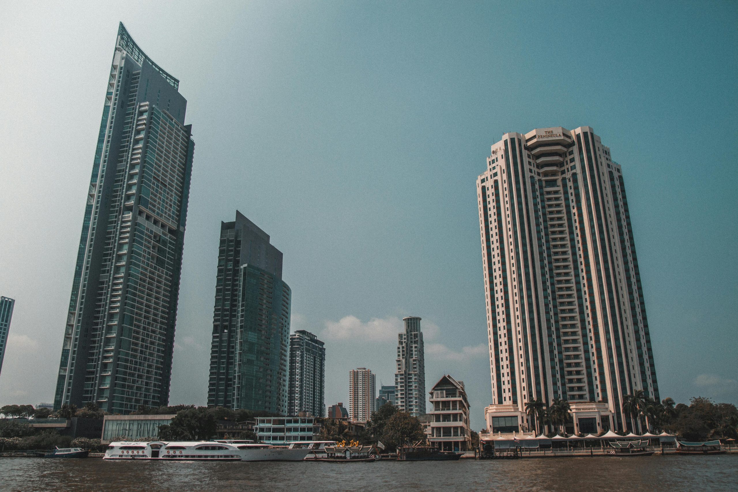 Panoramic view of Bangkok's waterfront with skyscrapers under a clear sky.